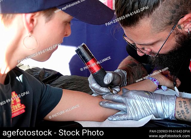 PRODUCTION - 02 September 2023, Bavaria, Munich: Artist from Tattooine-sayagata tattoos a visitor at the ""Superbloom"" festival in Munich