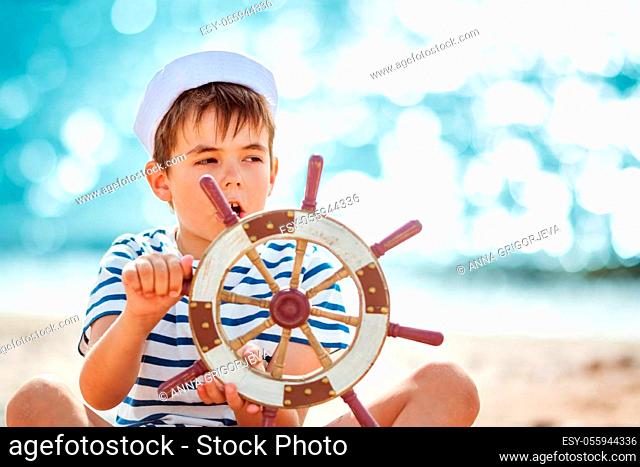 seven years old boy playing at the beach in sailor hat. Child with a steering wheel at sea