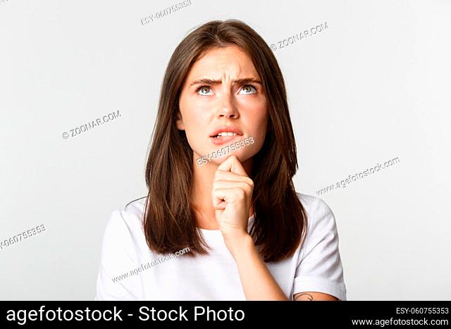 Close-up of puzzled cute thoughtful girl looking up and thinking, standing white background and pondering decision