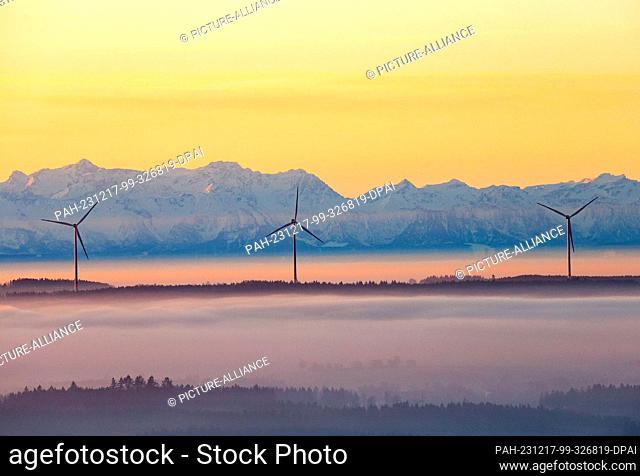 dpatop - 17 December 2023, Baden-Württemberg, Uttenweiler: Three wind turbines rise out of the fog in the morning shortly after sunrise, while the Alps