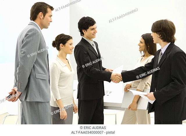 Business associates meeting, shaking hands while others watch