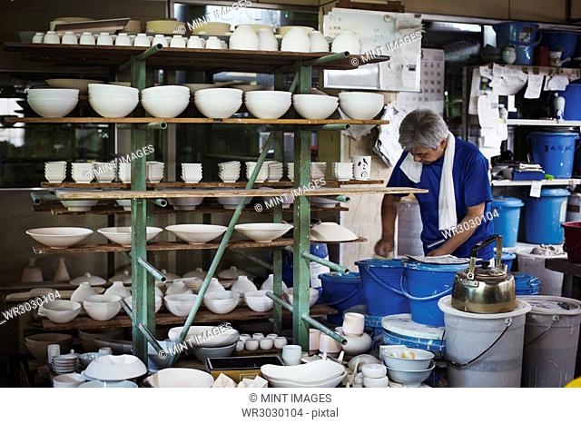 Man standing in a Japanese porcelain workshop with shelves of various porcelain bowls