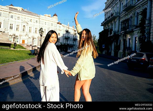 Cheerful friends holding hands during sunny day