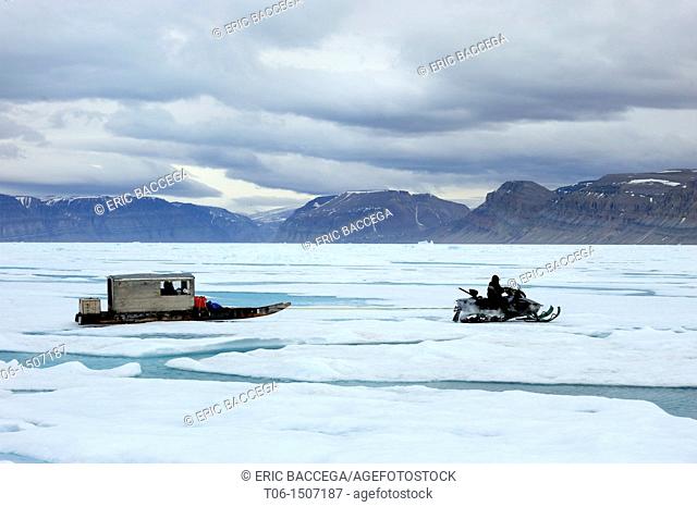 Inuit hunter driving snowmobile with Qamutik Inuit sledge on icepack, Arctic Bay, Baffin Island, Nunavut, Canada
