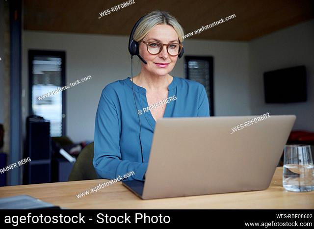 Smiling woman wearing eyeglasses using laptop at home