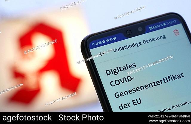 26 January 2022, ---: ILLUSTRATION - A man holds up his smartphone with the digital Covid recovery certificate in front of a pharmacy logo