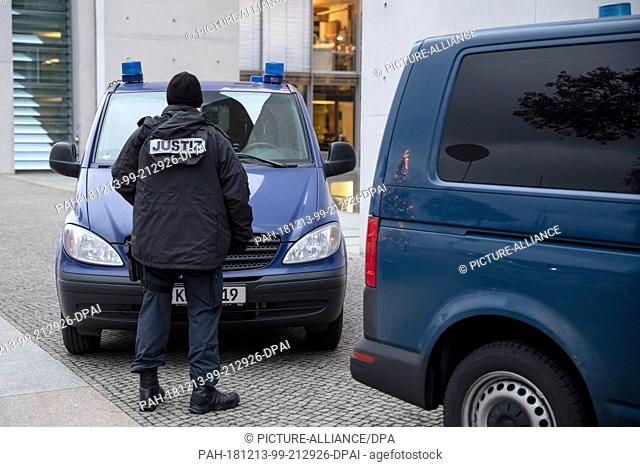13 December 2018, Berlin: A justice official stands next to two vehicles at the Paul-Löbe-Haus. On Thursday, members of the Bundestag questioned a Moroccan