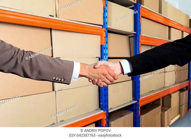 Partners Shaking Hands In Front Of Cargo Shelves