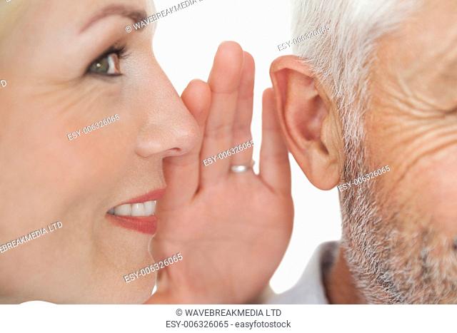 Close up of a woman whispering secret into a man's ear over white background