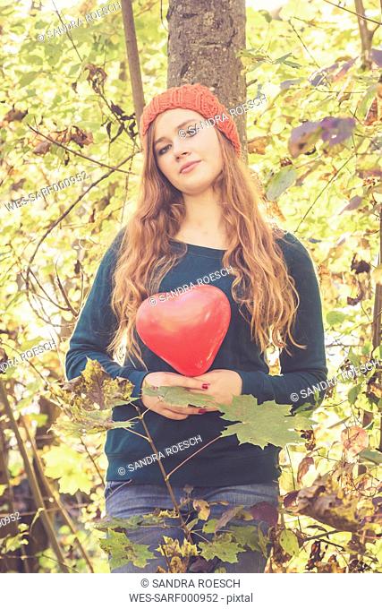 Teenage girl with heart shaped balloon leaning at a tree