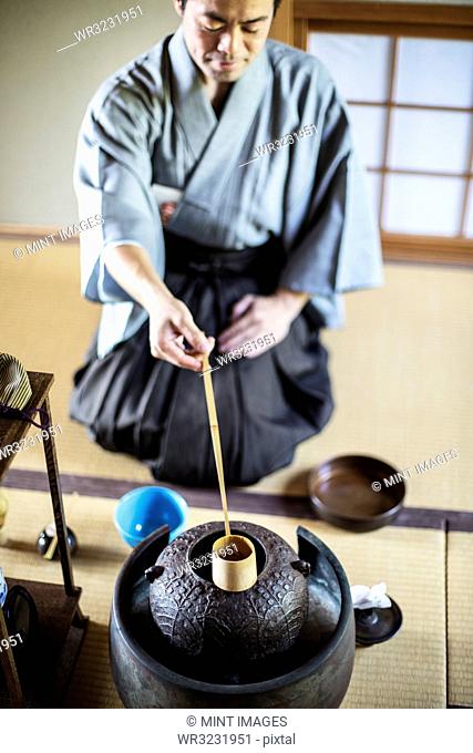 Traditional Japanese Tea Ceremony, man wearing kimono sitting on floor, using a Hishaku, a bamboo ladle, to pour hot water