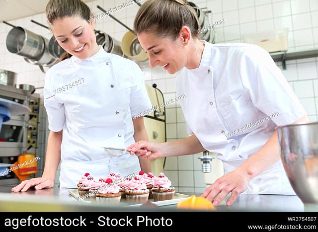 Two baker women in pastry bakery working on muffins together