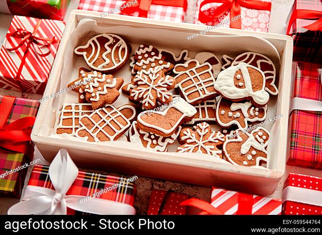 Delicious fresh Christmas decorated gingerbread cookies placed in wooden crate. Wrapped gifts on sides. White rusty background. Top view