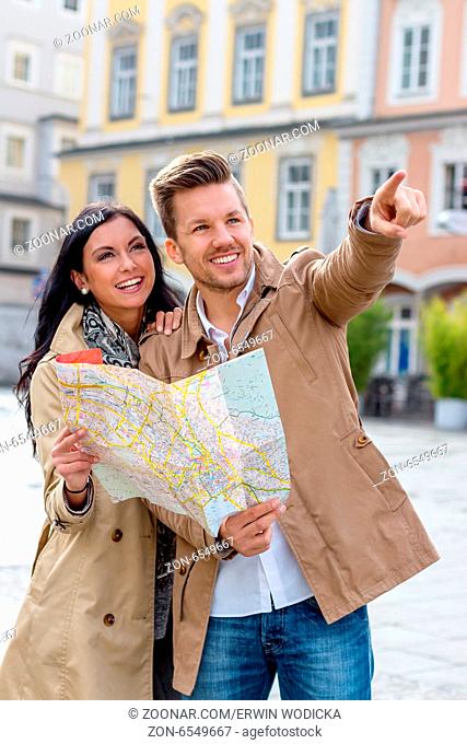 Junges Paar mit Stadtplan und Reiseführer bei der Besichtigung einer Stadt im Urlaub