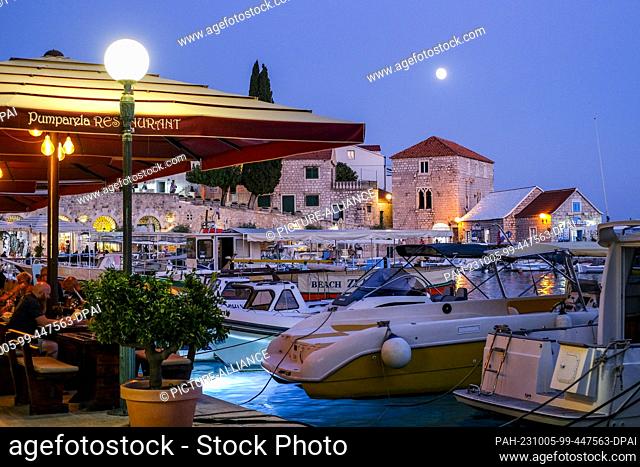 PRODUCTION - 27 September 2023, Croatia, Bol: The harbor with boats, cafes and restaurants in Bol on the island of Brac in the evening