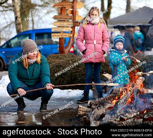 12 February 2023, Saxony-Anhalt, Stolberg: Visitors sit in front of the Josephskreuz on the Auerberg by the fire and bake stick bread