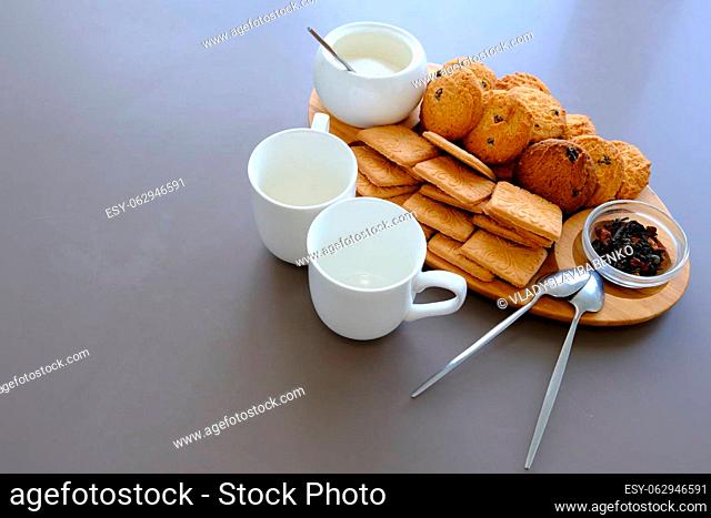 A tasty snack two cups of black tea and a plate of oatmeal cookies a wooden board on the gray background, leaf tea