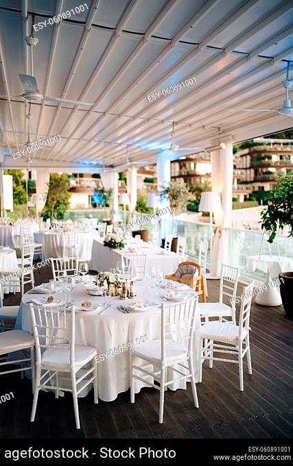 Round banquet table with white tablecloth and white Chiavari chairs. Wedding under the tent