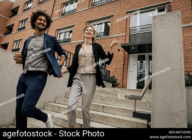 Happy couple holding hands walking down stairs of apartment building