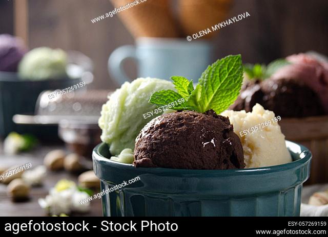 Three scoops of Vanilla pistachio and chocolate icecream balls in clay bowls on wooden kitchen table