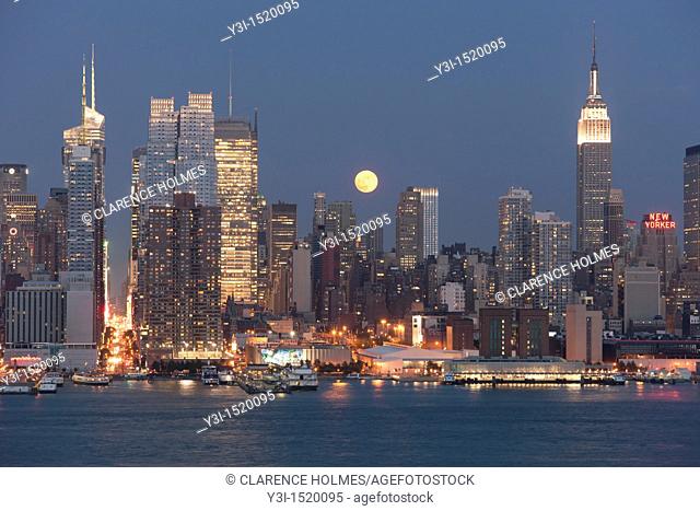 The full moon rises over the Manhattan skyline at twilight as viewed over the Hudson River from New Jersey