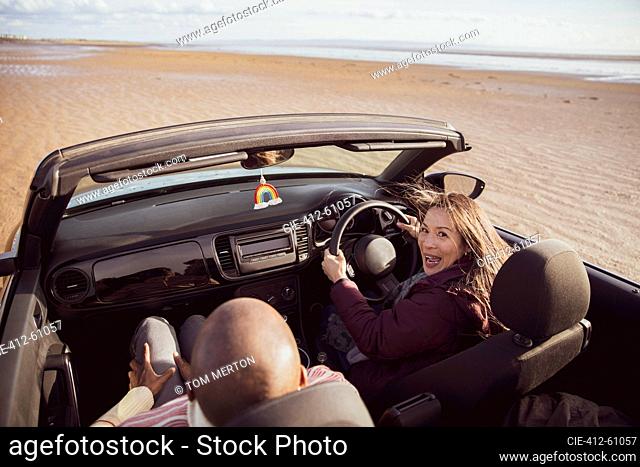 Portrait happy couple driving convertible on sunny beach