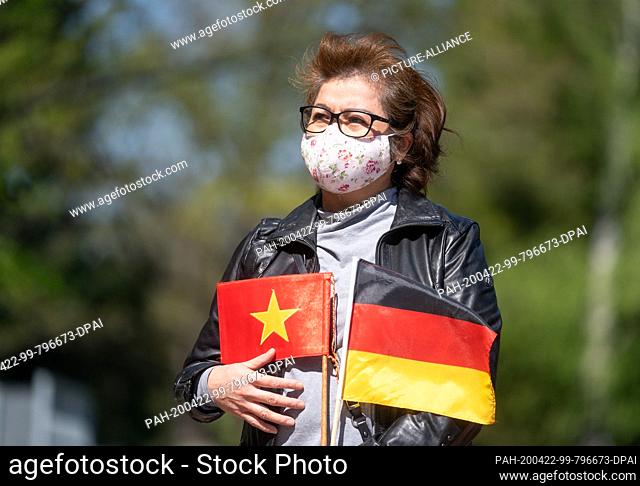 22 April 2020, Saxony, Dresden: A member of the Vietnamese community stands with a small Vietnamese and a German flag at a senior citizens' residence in Dresden