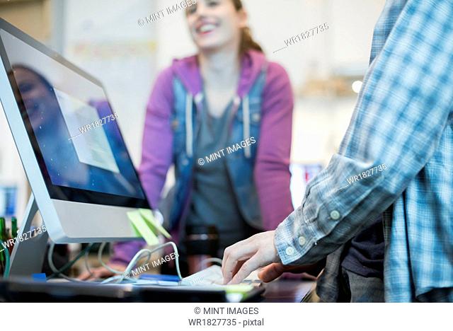 Two people at a computer repair shop, one typing and checking a monitor display