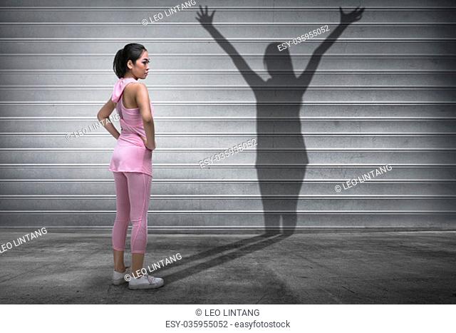 Young asian fitness woman with a shadow of spirit on metal roller shutter