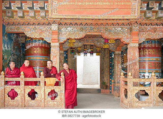 Four monks in red robes, ornate wooden wall, Buddhist Tango Goemba Monastery near Thimphu, Kingdom of Bhutan