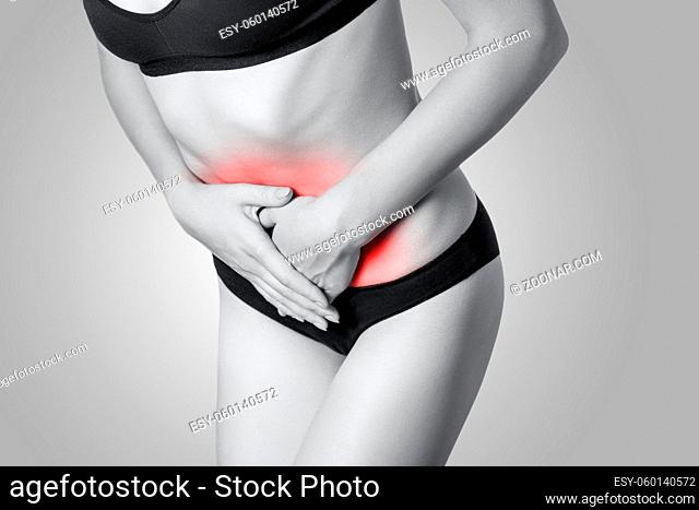 Closeup view of a young woman with stomach pain or digestion or period cycle on gray background. Black and white photo with red dot