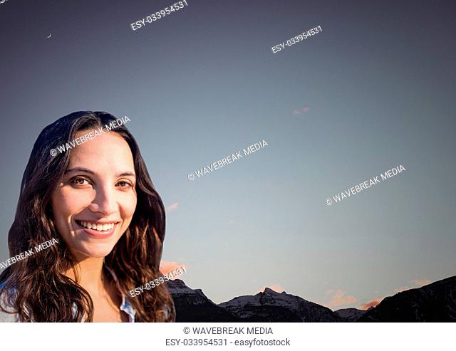Millennial woman smiling against mountain tops and evening sky