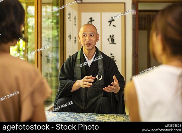 Two Japanese women and Buddhist priest kneeling in Buddhist temple, talking