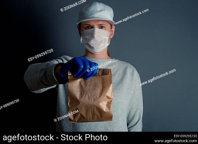Safe food or goods delivery. Young courier delivering small brown eco paper bag order to the home of customer with mask and gloves during the coronavirus...