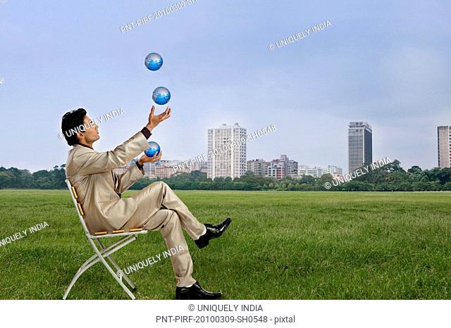 Businessman juggling with globes in a park with city skyline in the background