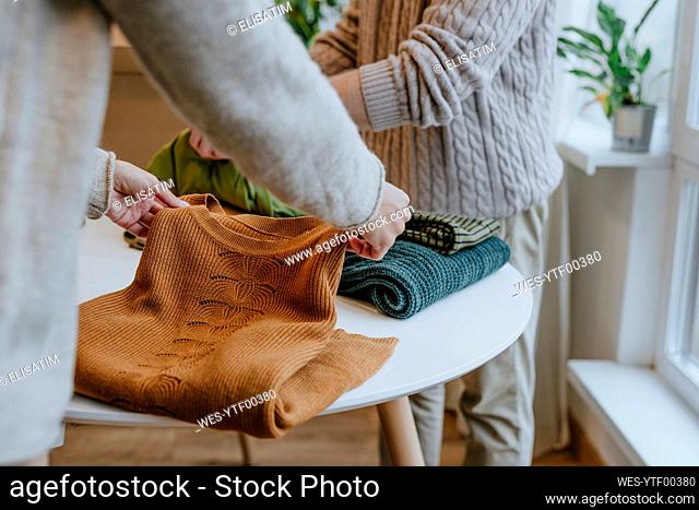 Young fashion designer with colleague folding clothes on table