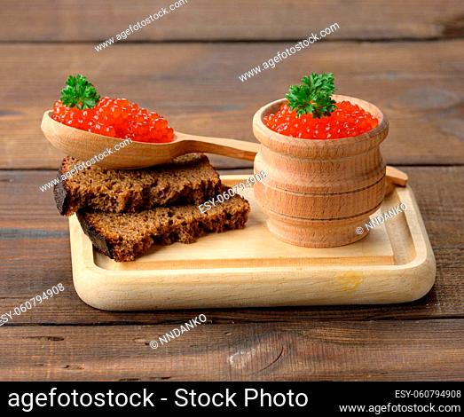 red salmon caviar lies on a piece of rye bread. Brown wooden table
