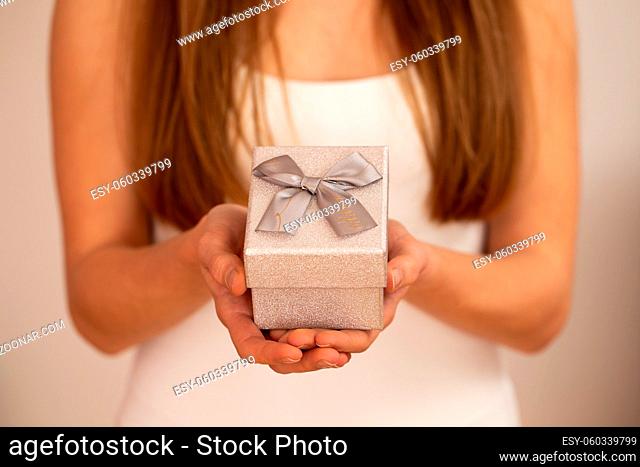 Woman holding little silver box with ribbon on white background. Blurred girl giving present from love. Blonde female showing small gift
