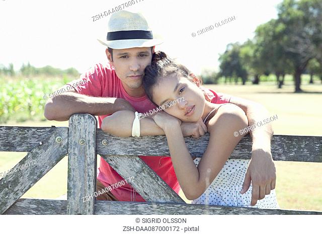 Young couple learning against wooden fence, portrait