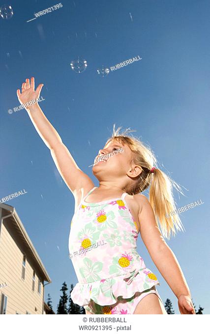 Girl in swimsuit catching bubbles outdoors with blue sky
