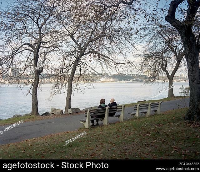 Elderly couple sitting on a bench in Riverside Park while watching the Hudson River, New York City