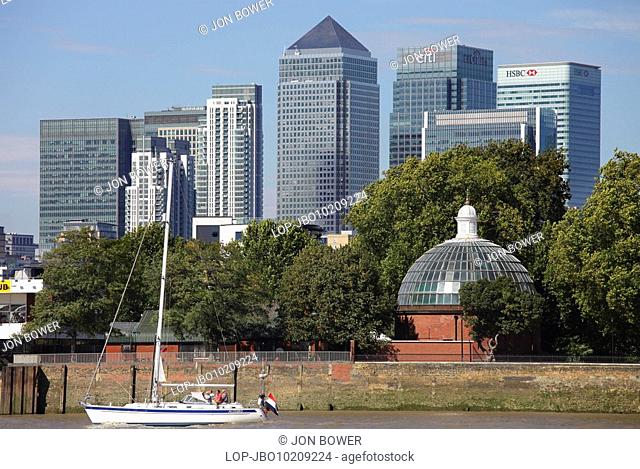 England, London, Isle of Dogs, A yacht sailing on the River Thames with the Canary Wharf development containing three of the UK's tallest buildings in the...