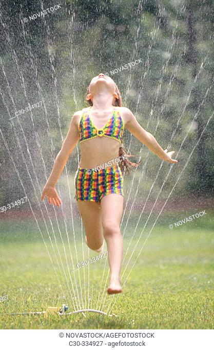 Girl running through lawn sprinkler on summer's day