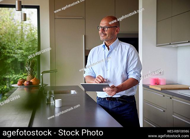 Smiling senior man with tablet PC standing by kitchen island at home