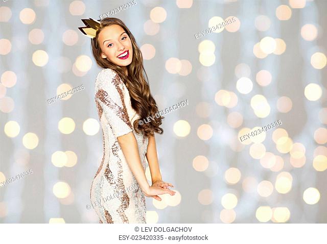 people, holidays and celebration concept - happy young woman or teen girl in party dress and princess crown over holidays lights background