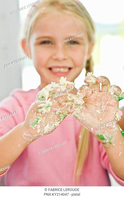 Portrait of a girl showing her messy hand covered with cake icing