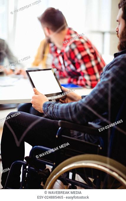 Colleague on wheelchair using digital tablet against photo editors