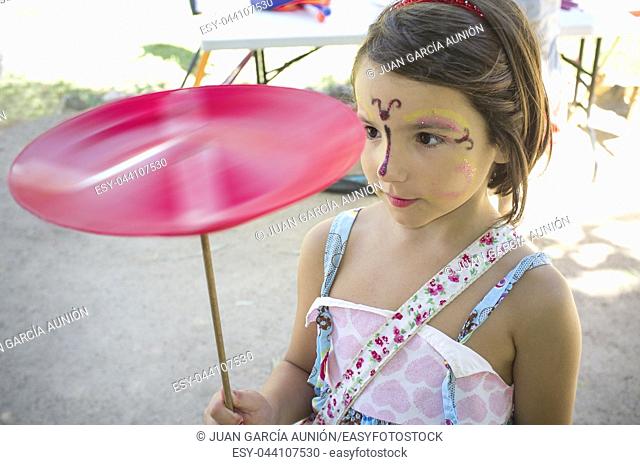 Face painted child girl playing with spinning plate. Classic toys concept