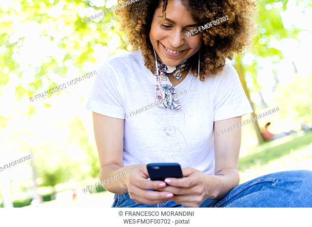 Smiling woman with cell phone and earphones in park