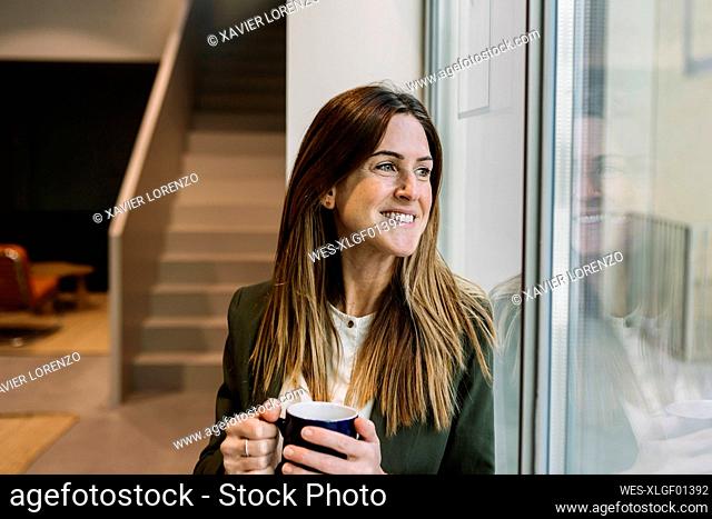 Thoughtful businesswoman with coffee mug looking through window at office